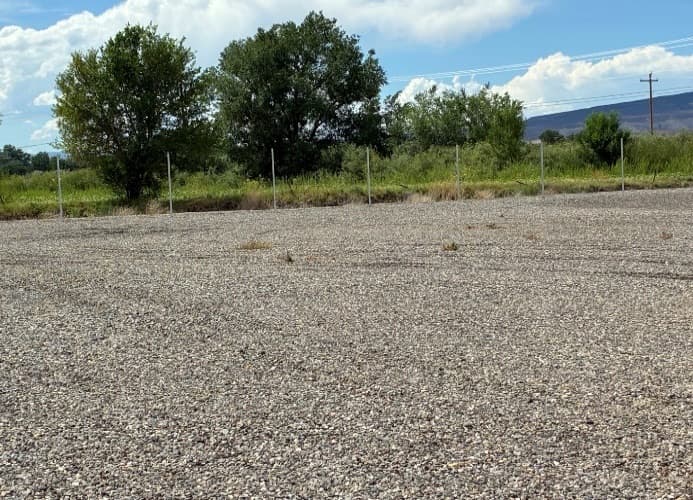 Fence posts set along the perimeter of the graded gravel lot
